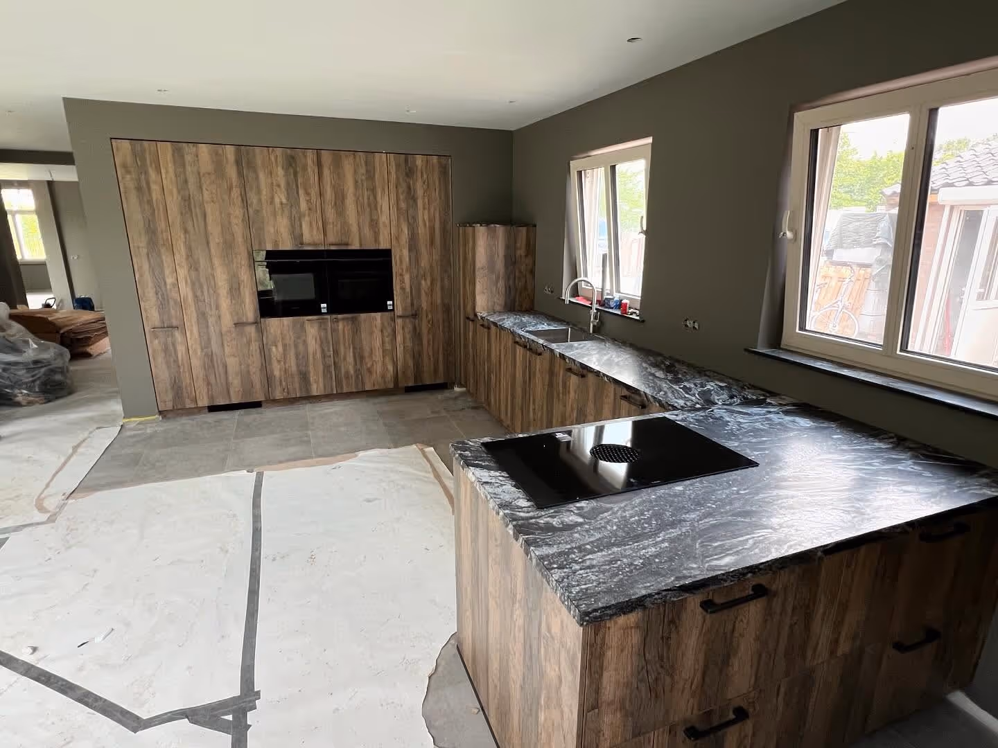 A modern dining room boasts an oval white table with wishbone chairs, a large round mirror above a woven buffet, and a vintage-style pendant light, all on a patterned rug.