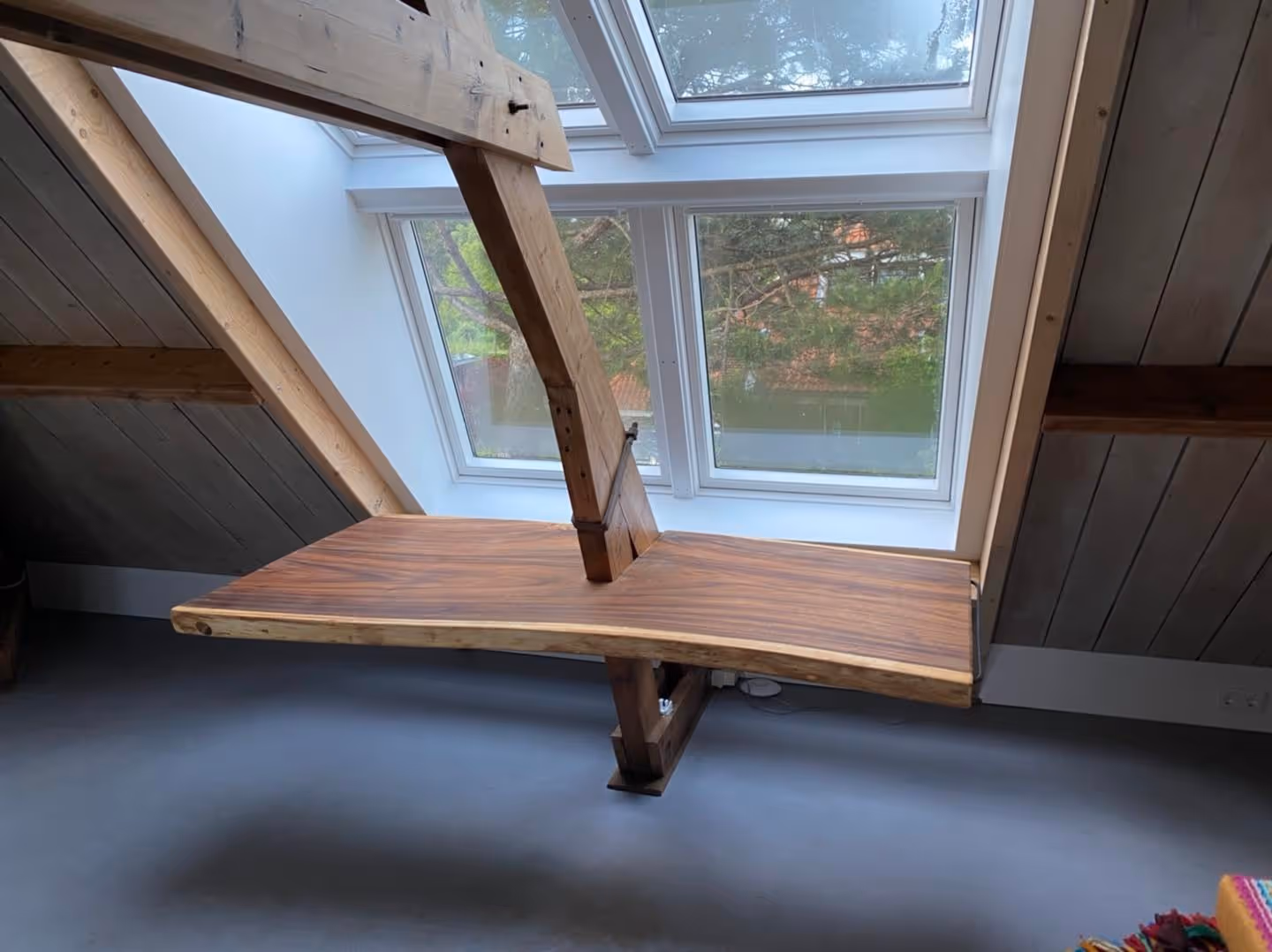 A gray dining room with a round black table, white chairs, and a geometric gold chandelier. To the left is a fireplace with stacked logs, and a doorway leads to another room.