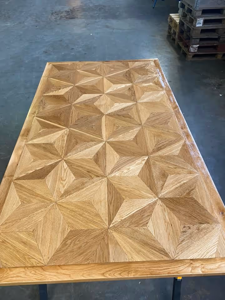 A cozy interior shot shows a black leather sofa next to a light wood open-shelf bench with a plant and books, below a light wood slatted staircase and a framed bird artwork.